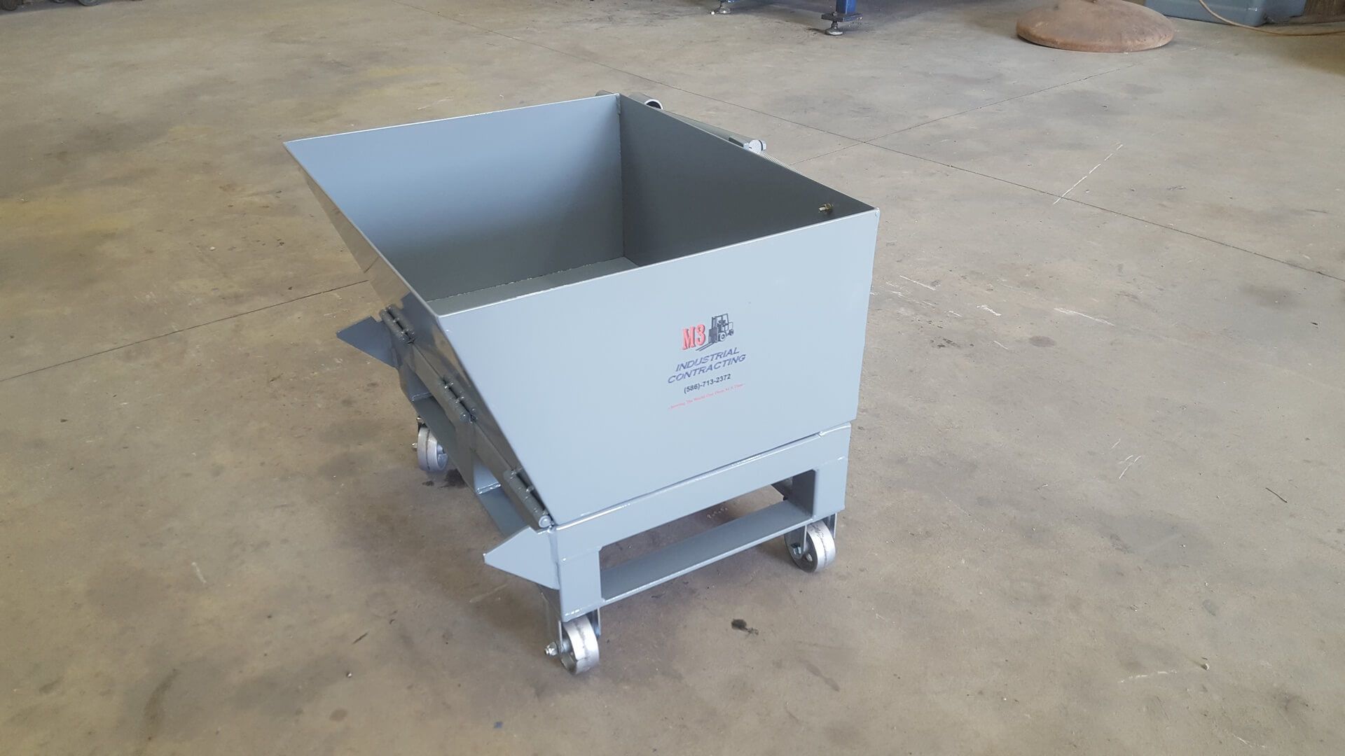 Gray metal hopper cart on wheels, angled, in an industrial setting.