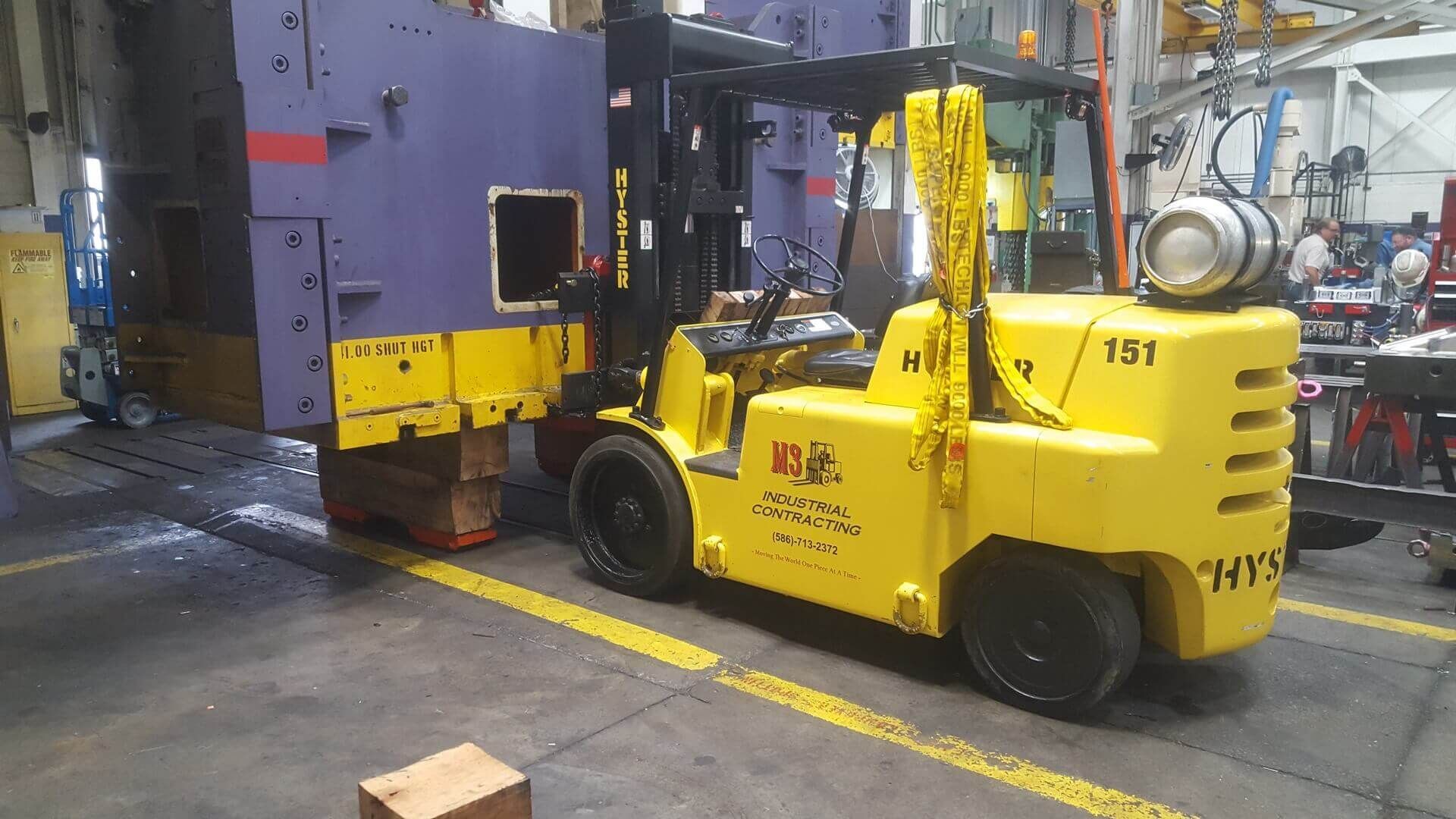 Yellow forklift next to a large purple industrial machine, indoors.