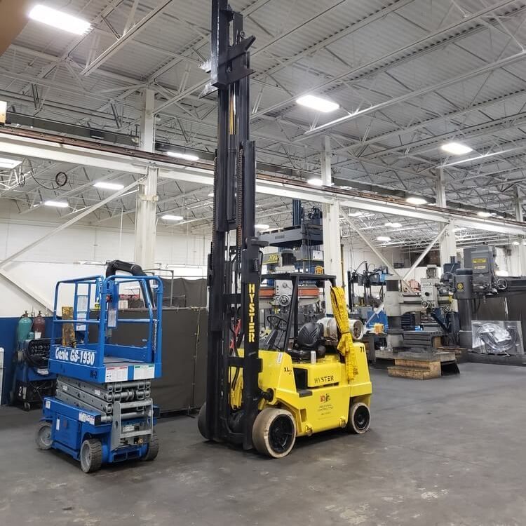 Yellow forklift and blue lift in a large industrial warehouse.