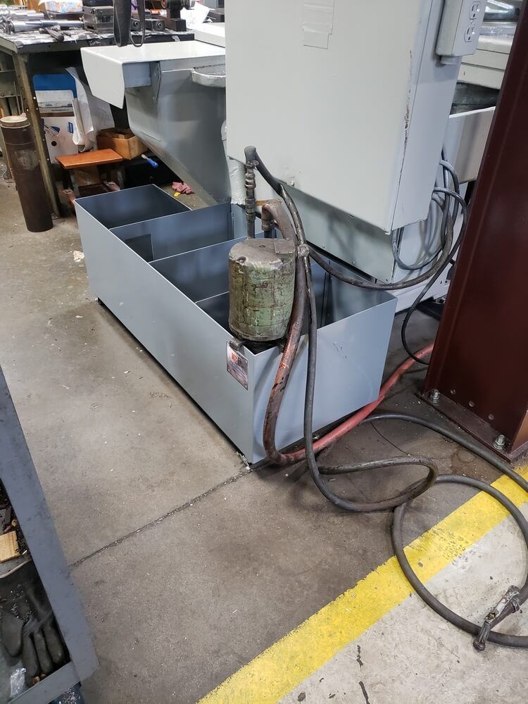 Metal industrial machine with coolant tank, power cords, and a yellow line on the floor.