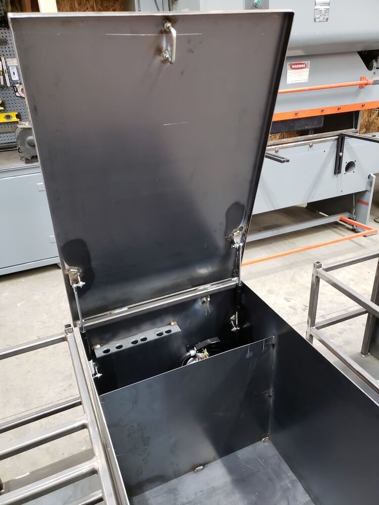 Open black metal box with hinged lid, inside is a divider. Shop environment.