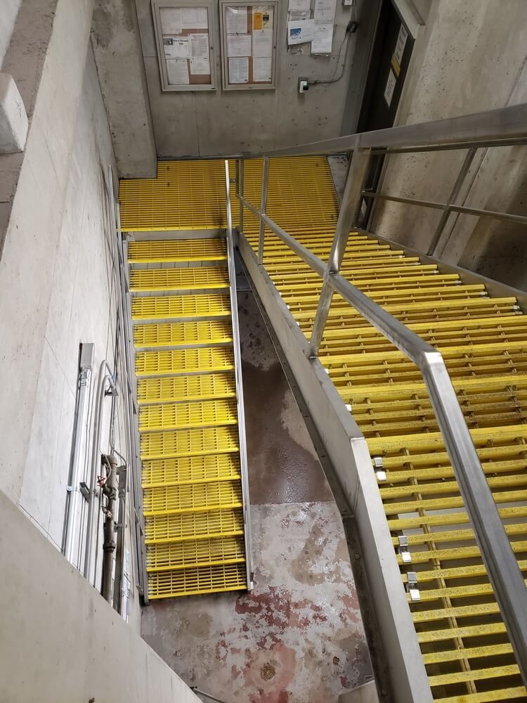 Staircase with yellow treads and metal handrails. Ascending in a concrete building, with information on the wall.