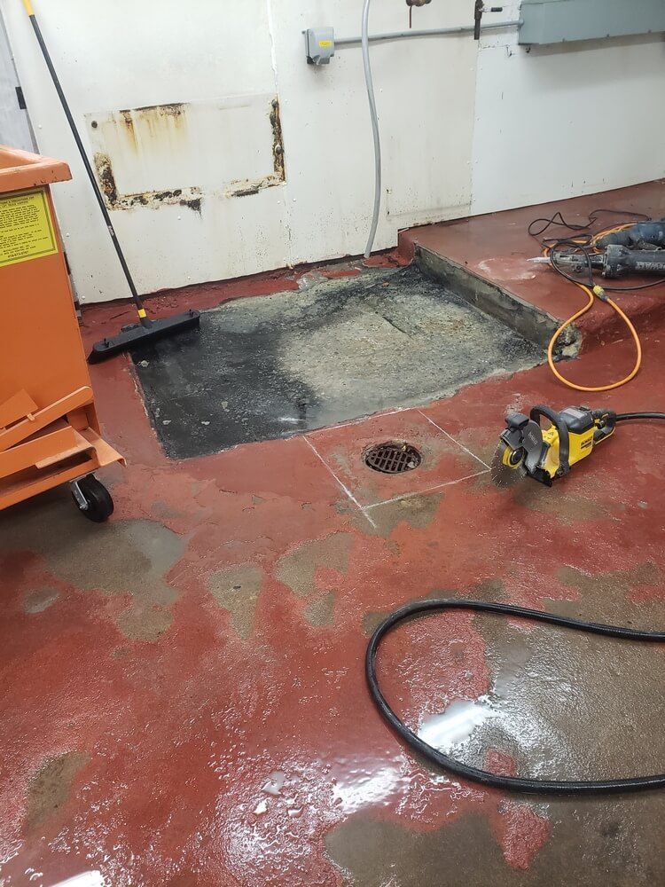 Red floor with cut-out section. A power saw and a hose lie nearby. A cart and broom are also in the room.
