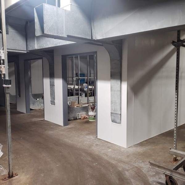 Interior construction: white walls, exposed ductwork, metal supports, and a view into a room with a window.