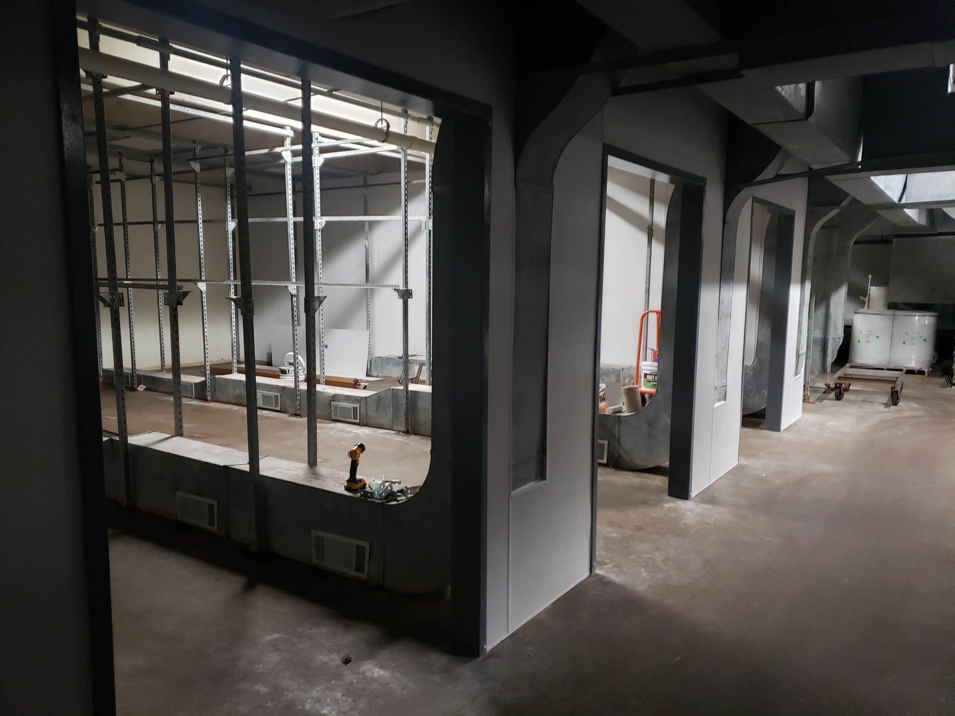 Interior under construction; walls and metal frames visible. Gray tones and concrete floor.