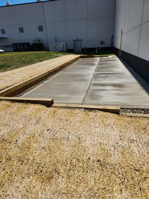 Concrete pad next to a building, framed by wood and gravel. Dry grass surrounds the area.