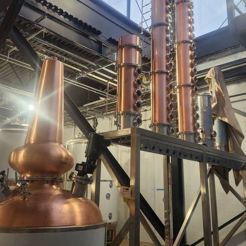 Copper stills and columns in a distillery, indoors, with steel support structure.