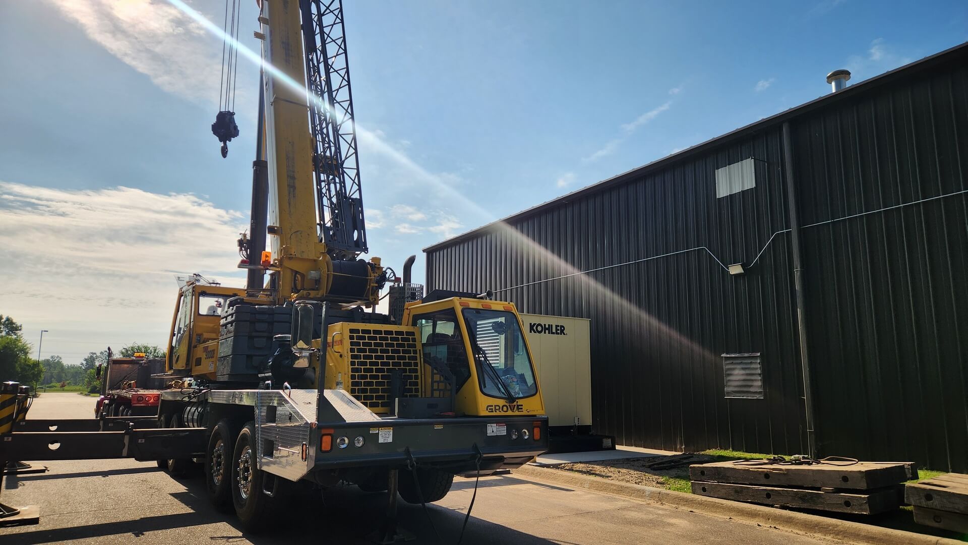 Yellow crane next to a dark building on a sunny day.