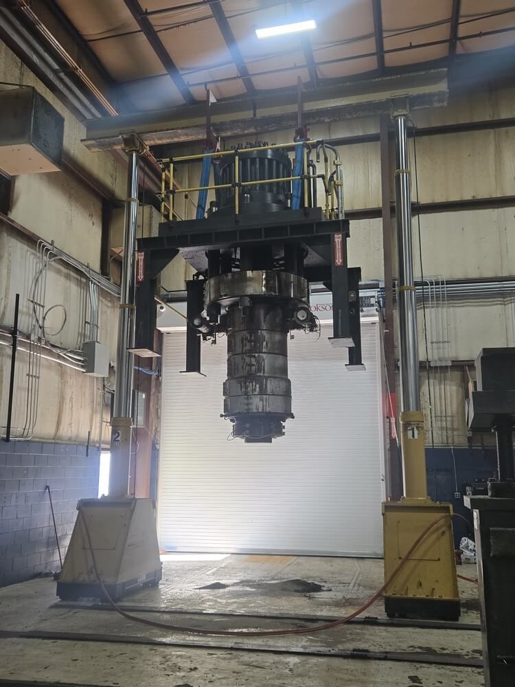 Industrial machinery suspended from overhead structure in a factory with a large door open behind it.