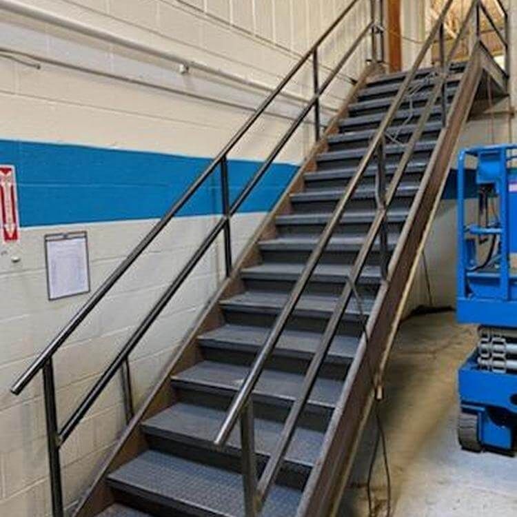 Metal staircase with handrails in an industrial setting, leading upward.