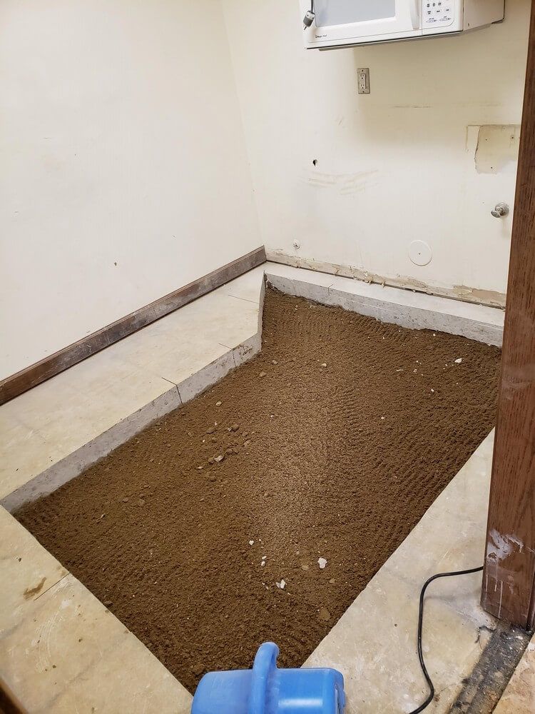 Room with sunken floor filled with brown material, framed by concrete and beige walls, microwave overhead.
