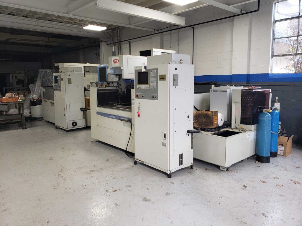 Machines in a workshop, possibly for manufacturing, with white exteriors and control panels. Blue cylinders are also visible.