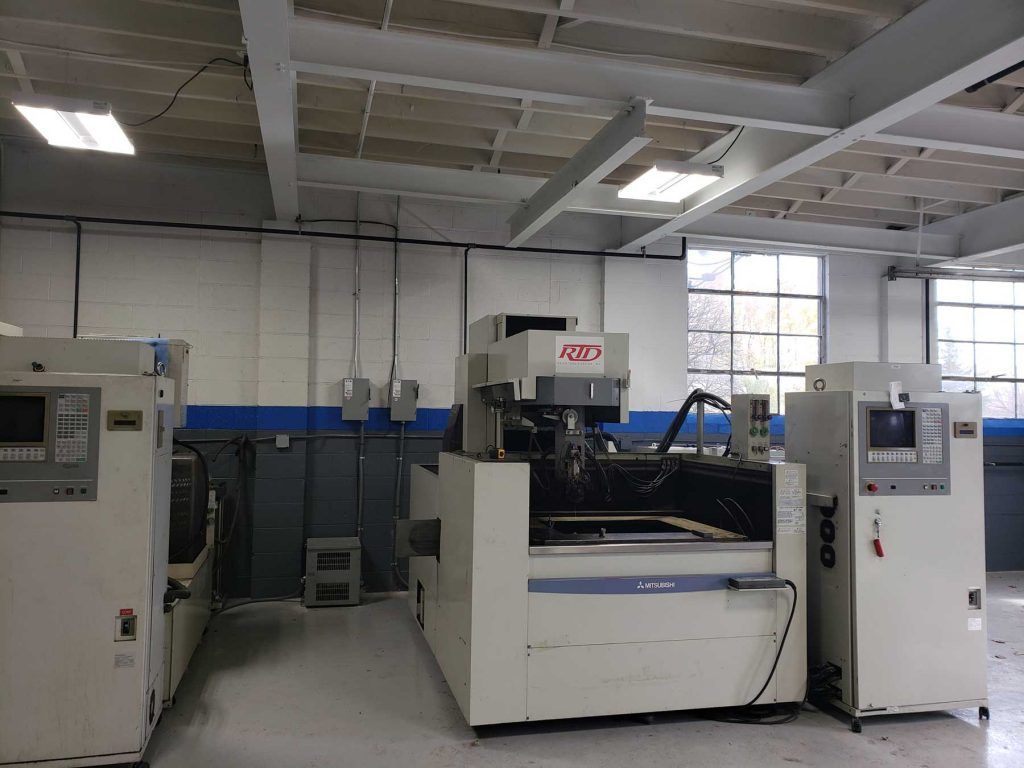 Machining workshop with three large industrial machines, white walls, and a fluorescent lighting.
