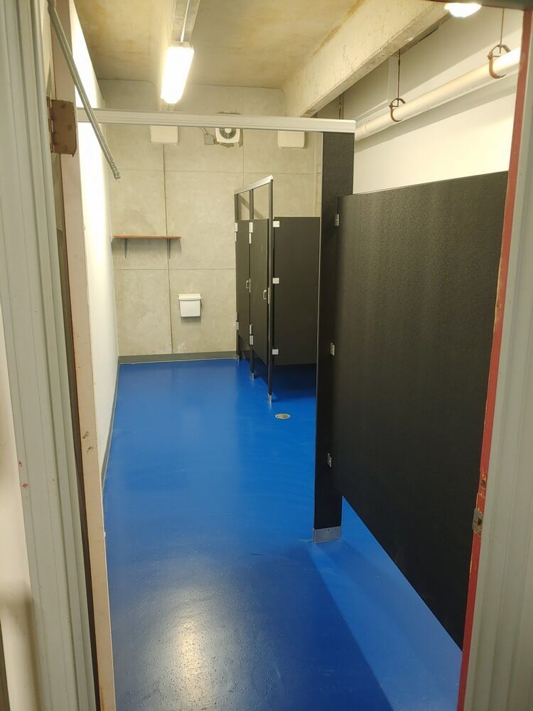 Blue-floored restroom with black stalls. A wall-mounted toilet paper dispenser and shelf are visible.