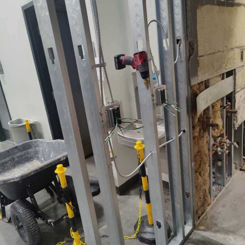 Construction site: metal studs, electrical tools, wheelbarrow with debris, caution poles.