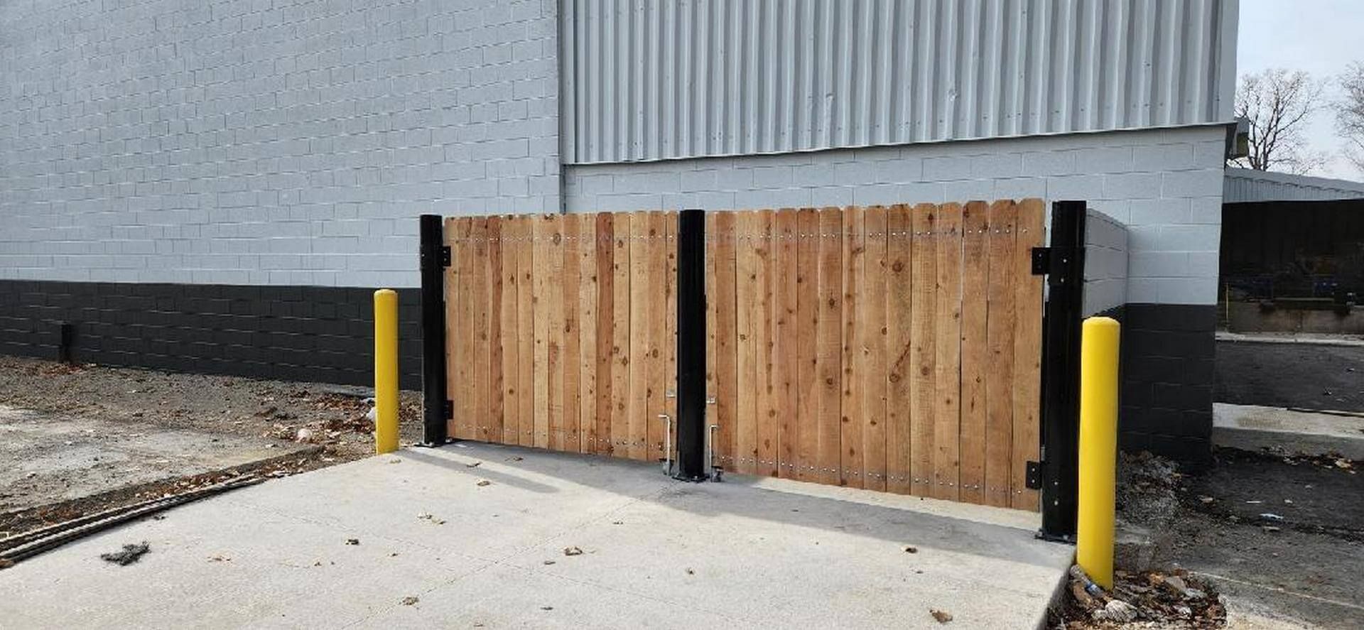 Wooden gate in front of a building with yellow bollards.
