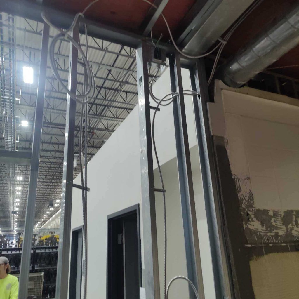 Metal framed wall with conduit and ductwork in an industrial setting. White walls, black door.