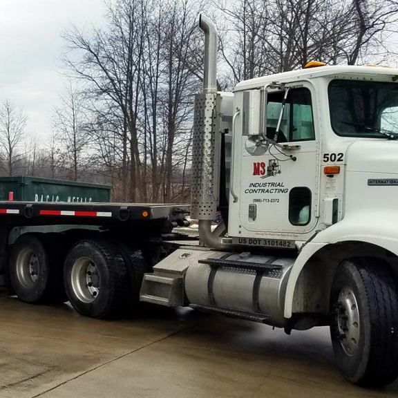 White semi-truck with a flatbed trailer; parked outdoors. The truck has the logo 