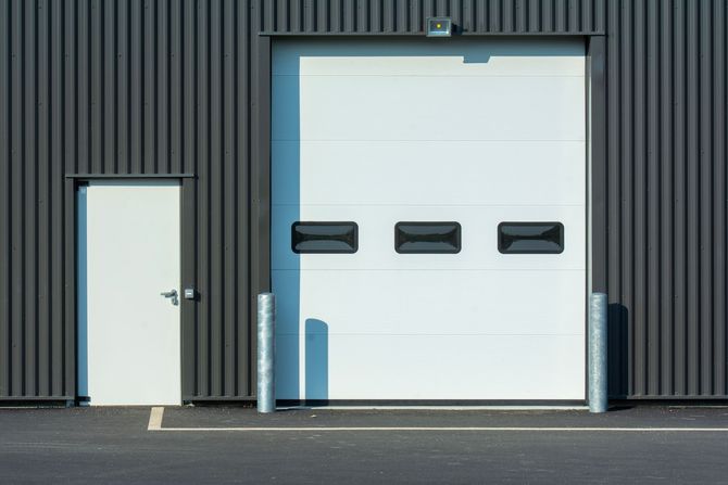 Industrial building facade with white door and large white garage door with three windows