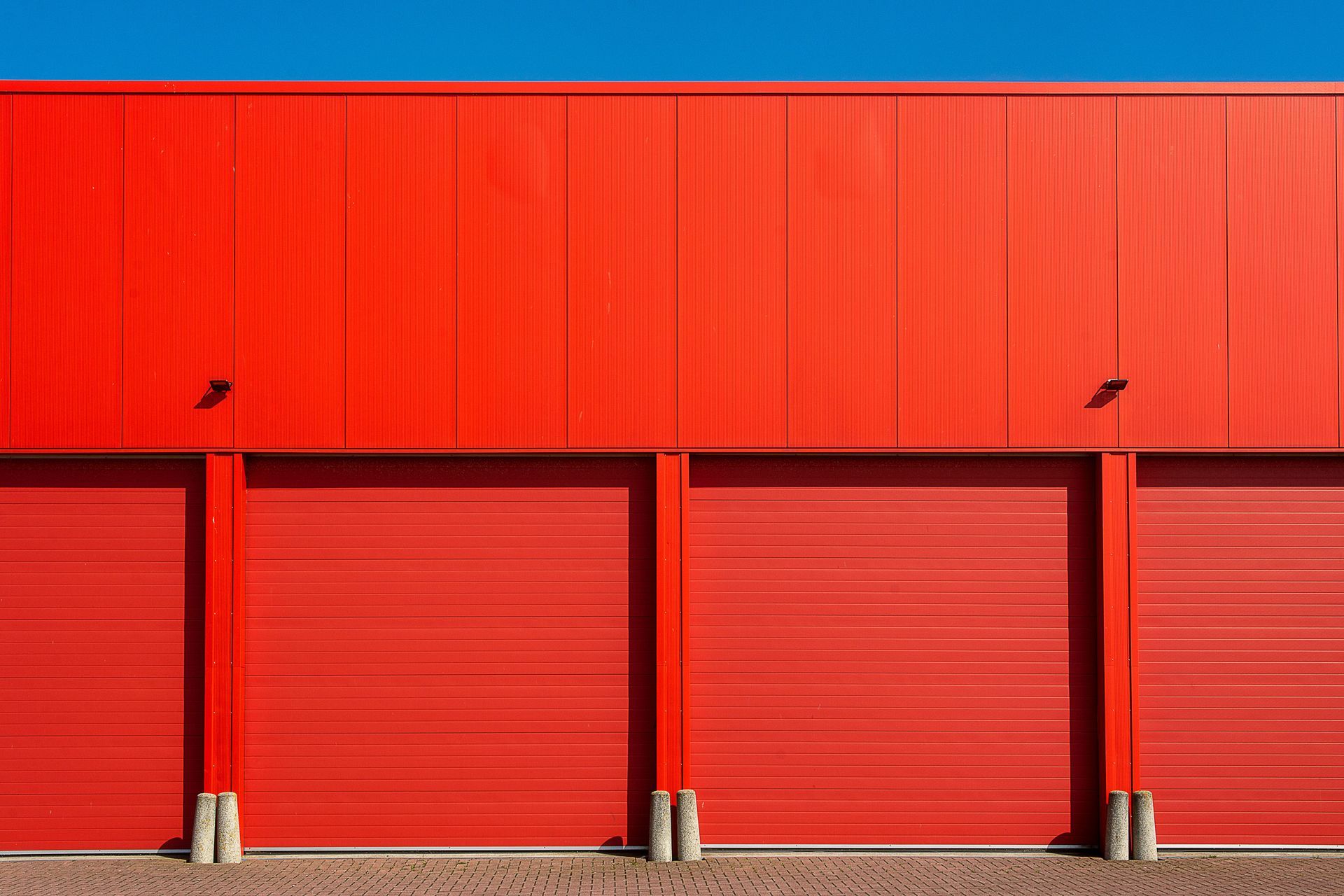 Red industrial building with four closed garage doors and small wall lights