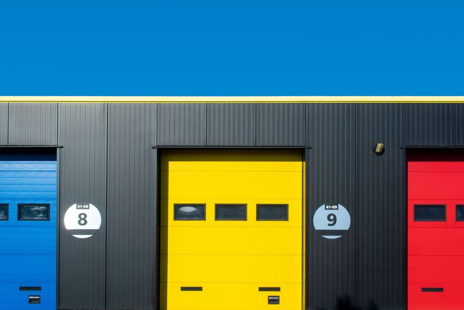 Colorful industrial warehouse doors: blue, yellow, and red bays with numbered signs on a dark building.