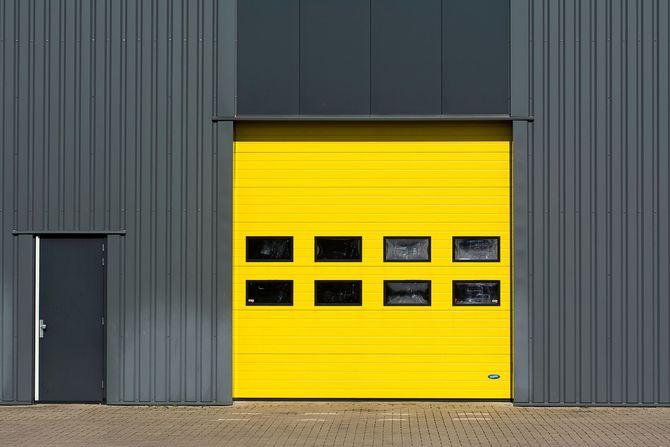 Gray industrial building with a bright yellow garage door and a small gray side door