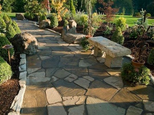 Stone garden path with plants and a bench in a sunny landscaped yard