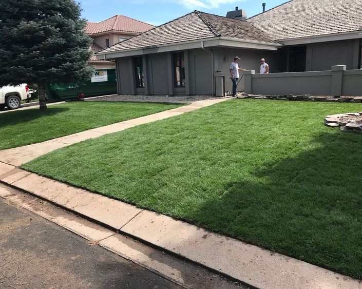 Suburban house with a green lawn and two people standing near the front patio.