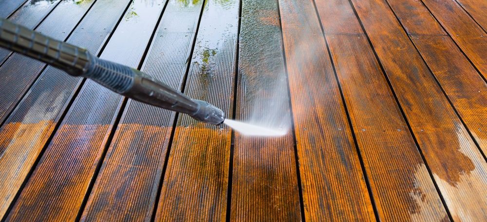 Pressure washer cleaning a wet wooden deck, revealing lighter wood beneath