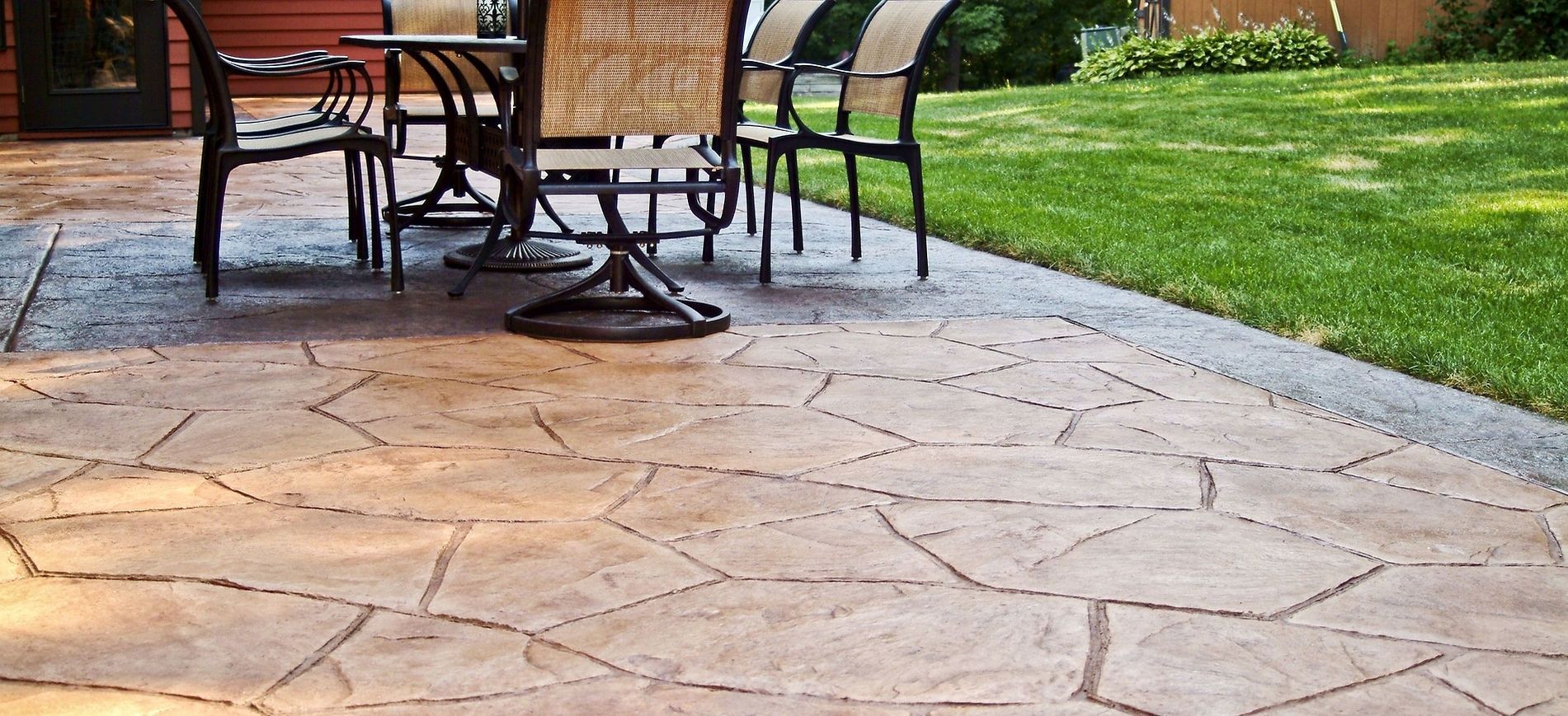 Stone patio with a metal table and chairs beside a green lawn