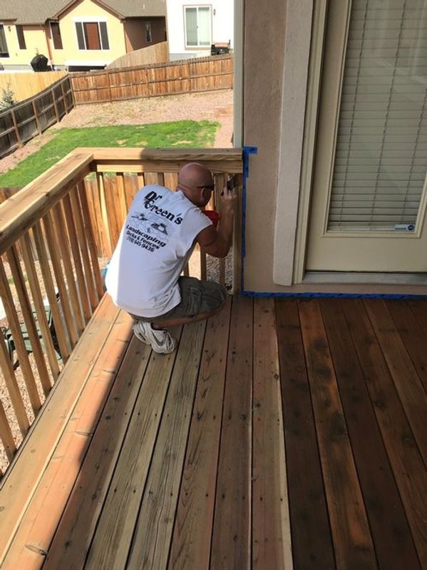Worker installing a blue fixture on a wooden deck beside a sliding door