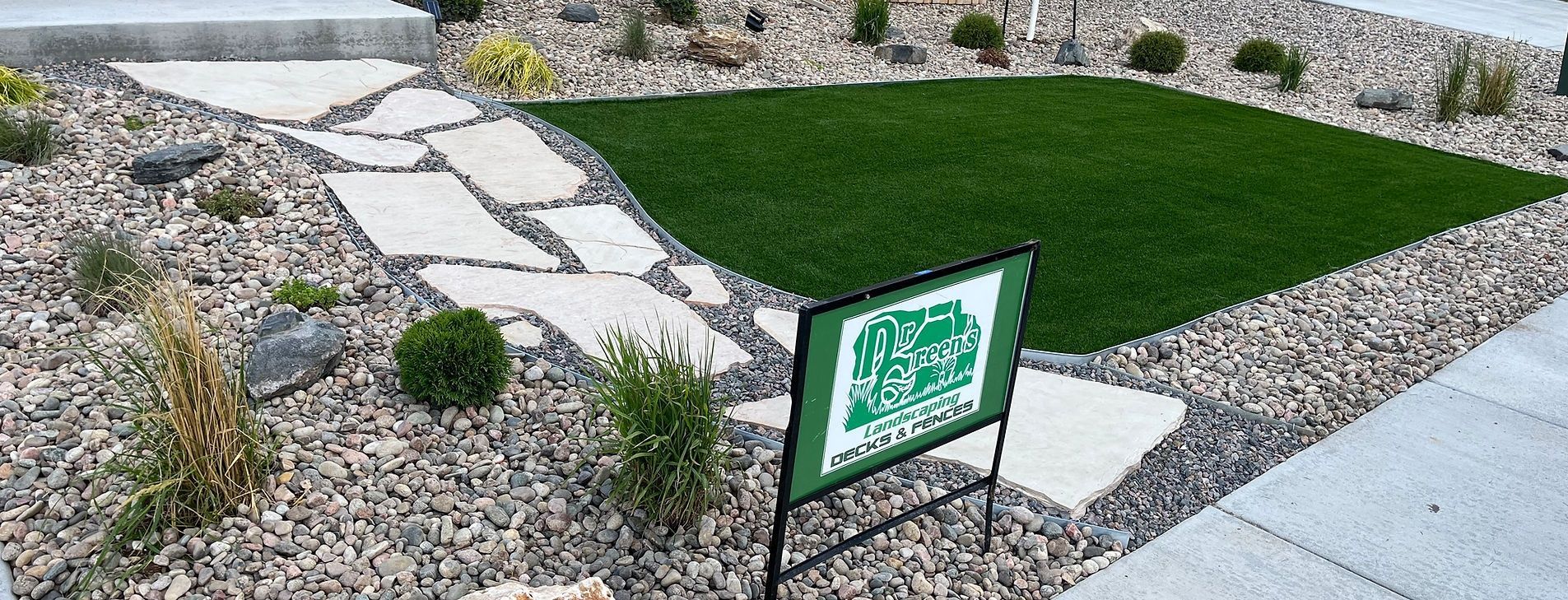 Front yard landscaping with stone walkway, gravel beds, and a green lawn sign by the sidewalk.