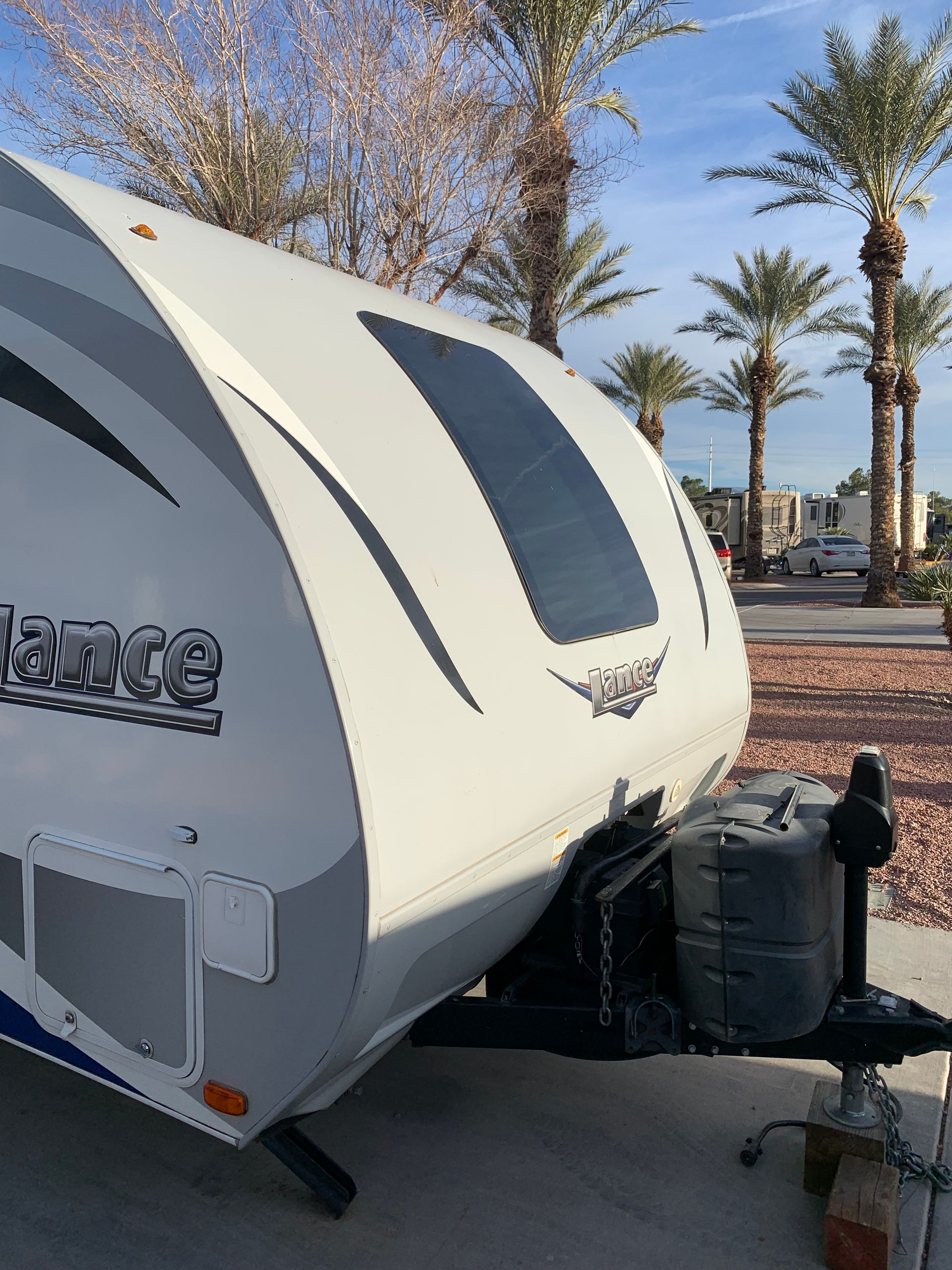 A white rv is parked in a parking lot with palm trees in the background.