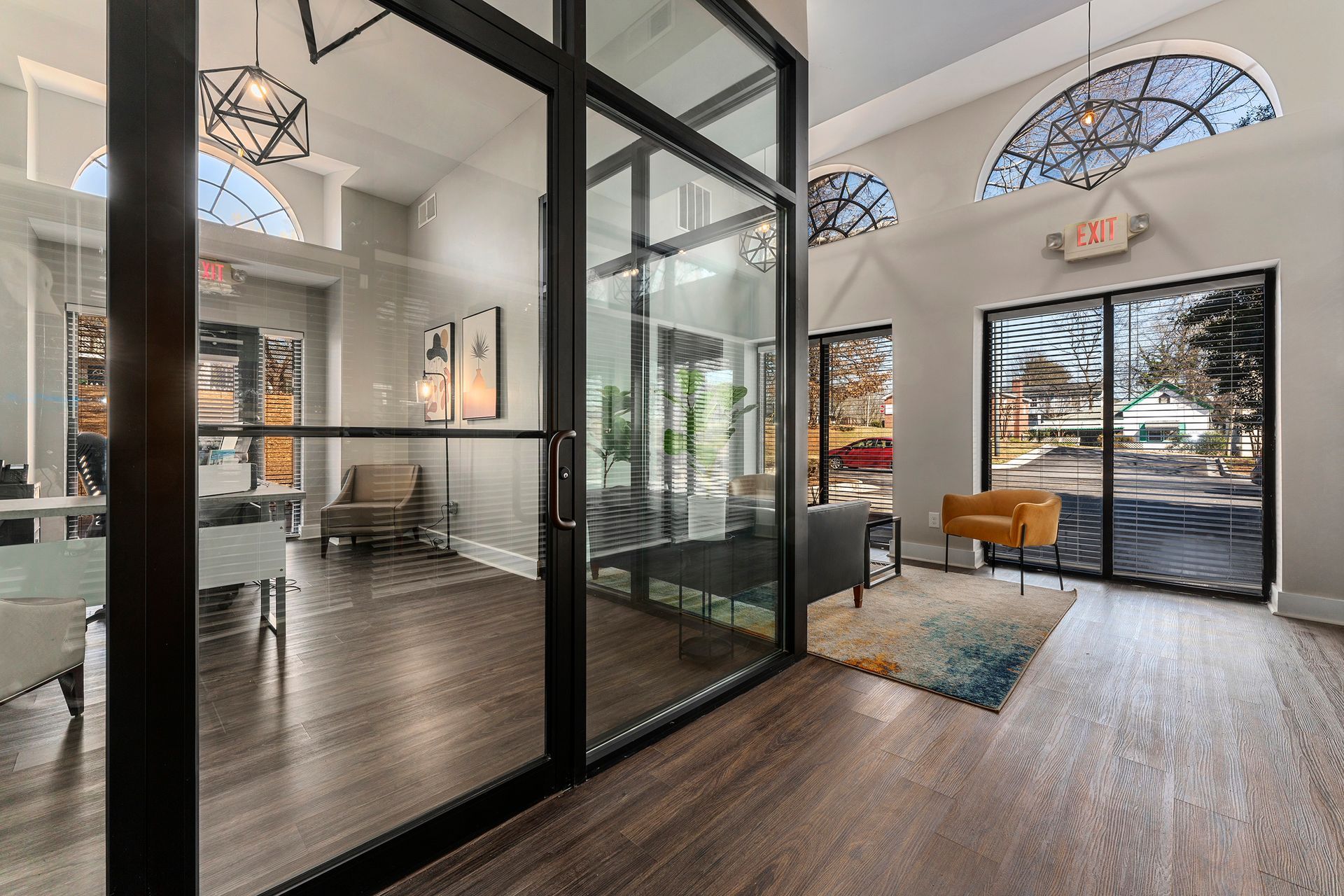 Modern lobby with glass-walled office, dark wood floors, lounge seating, and arched windows by the entrance