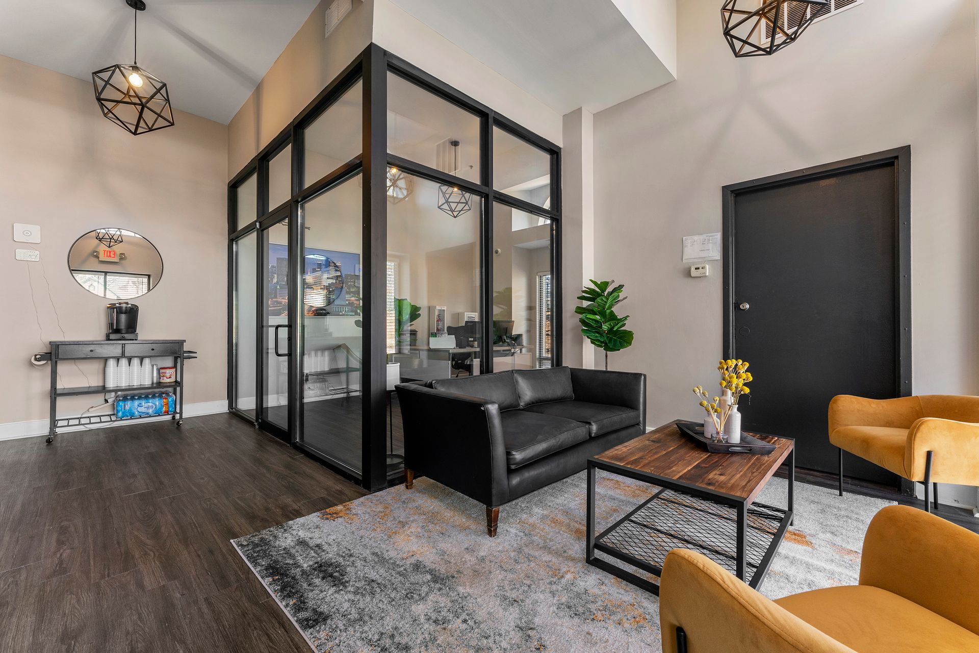 Modern office lounge with glass-walled room, black sofa, coffee table, and patterned rug on dark wood floors