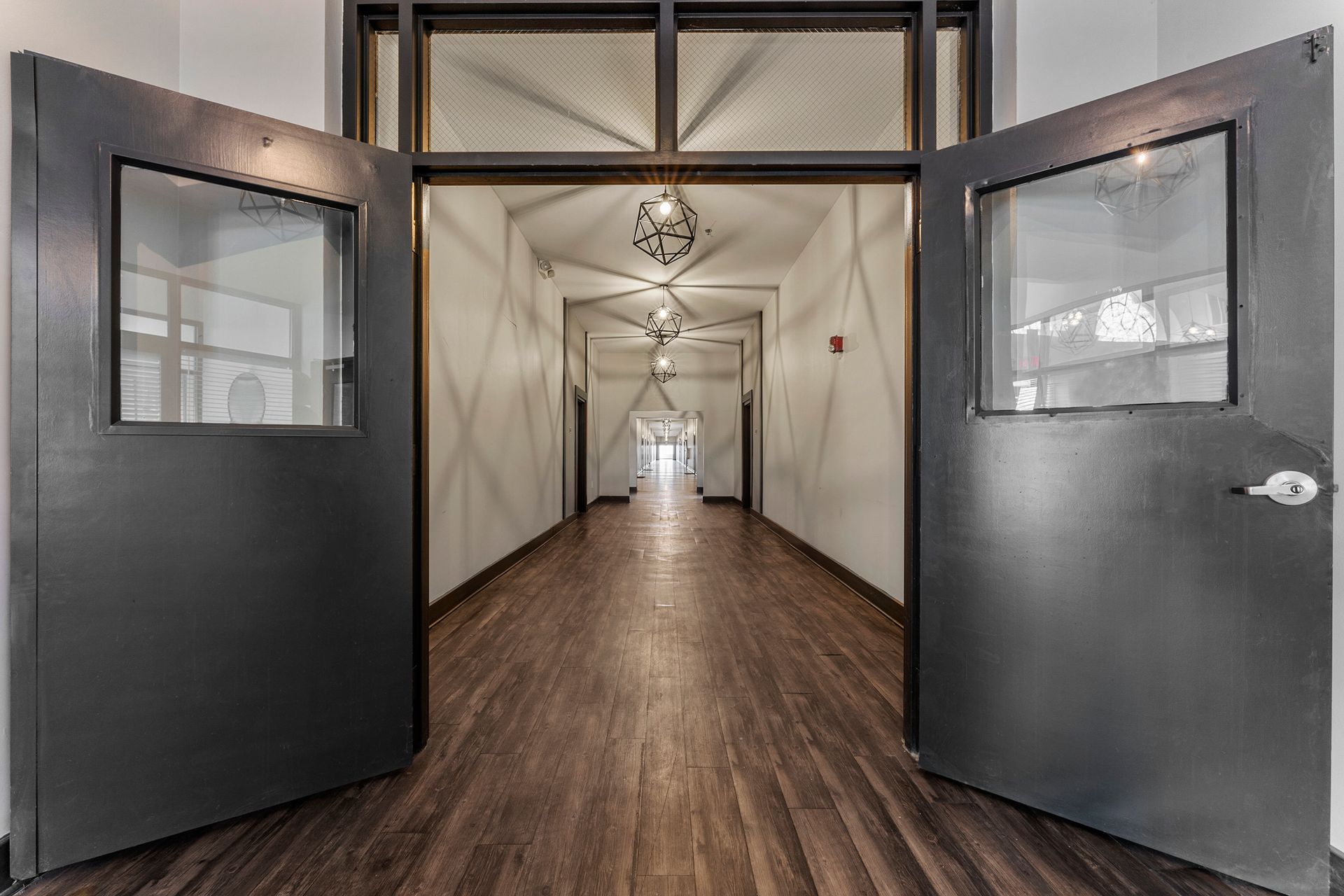 Open double doors to a long hallway with wood floors and hanging lights.