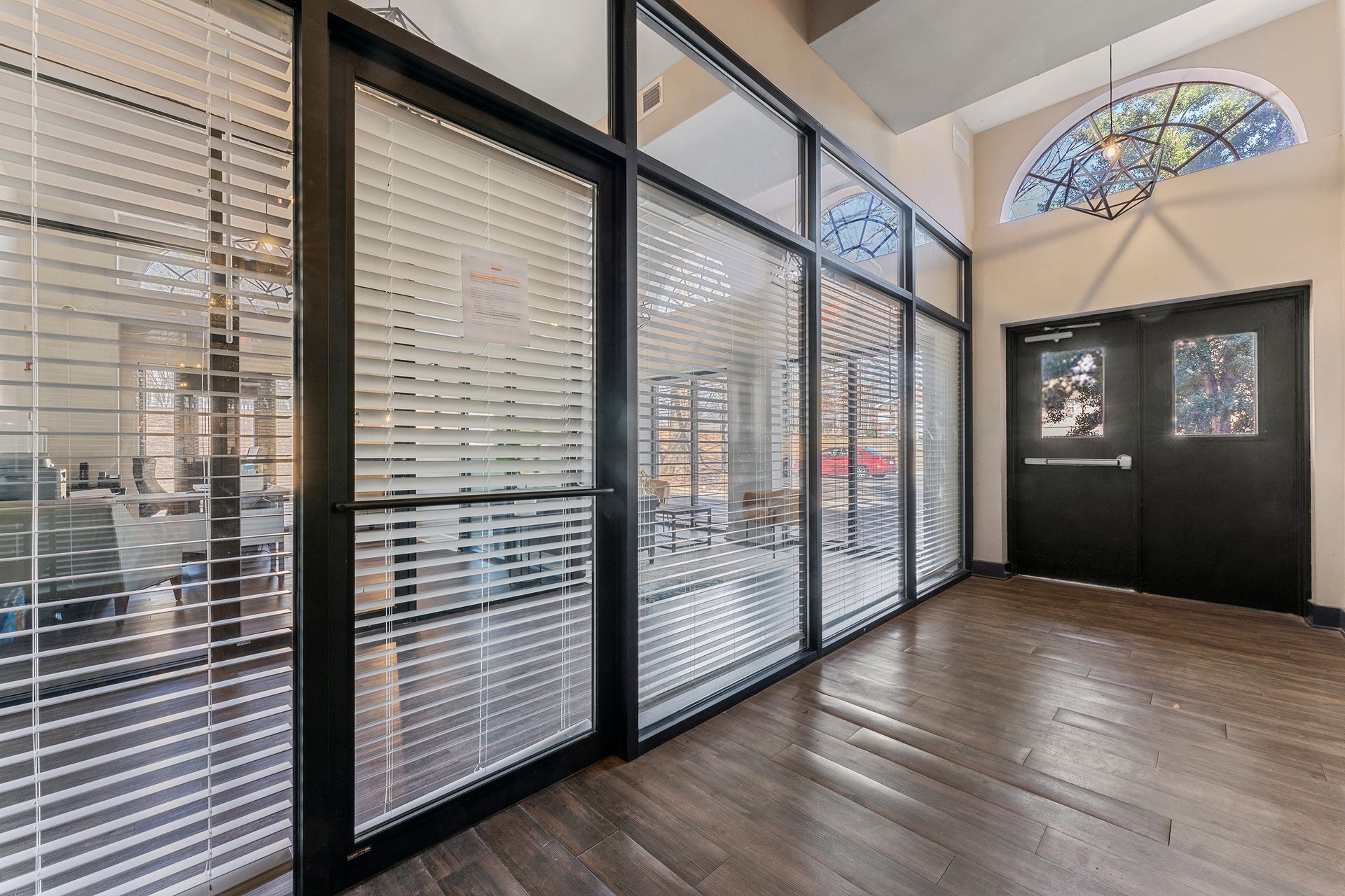 Bright lobby with glass partitions, blinds, wood floor, and double front doors under a stained-glass arch.