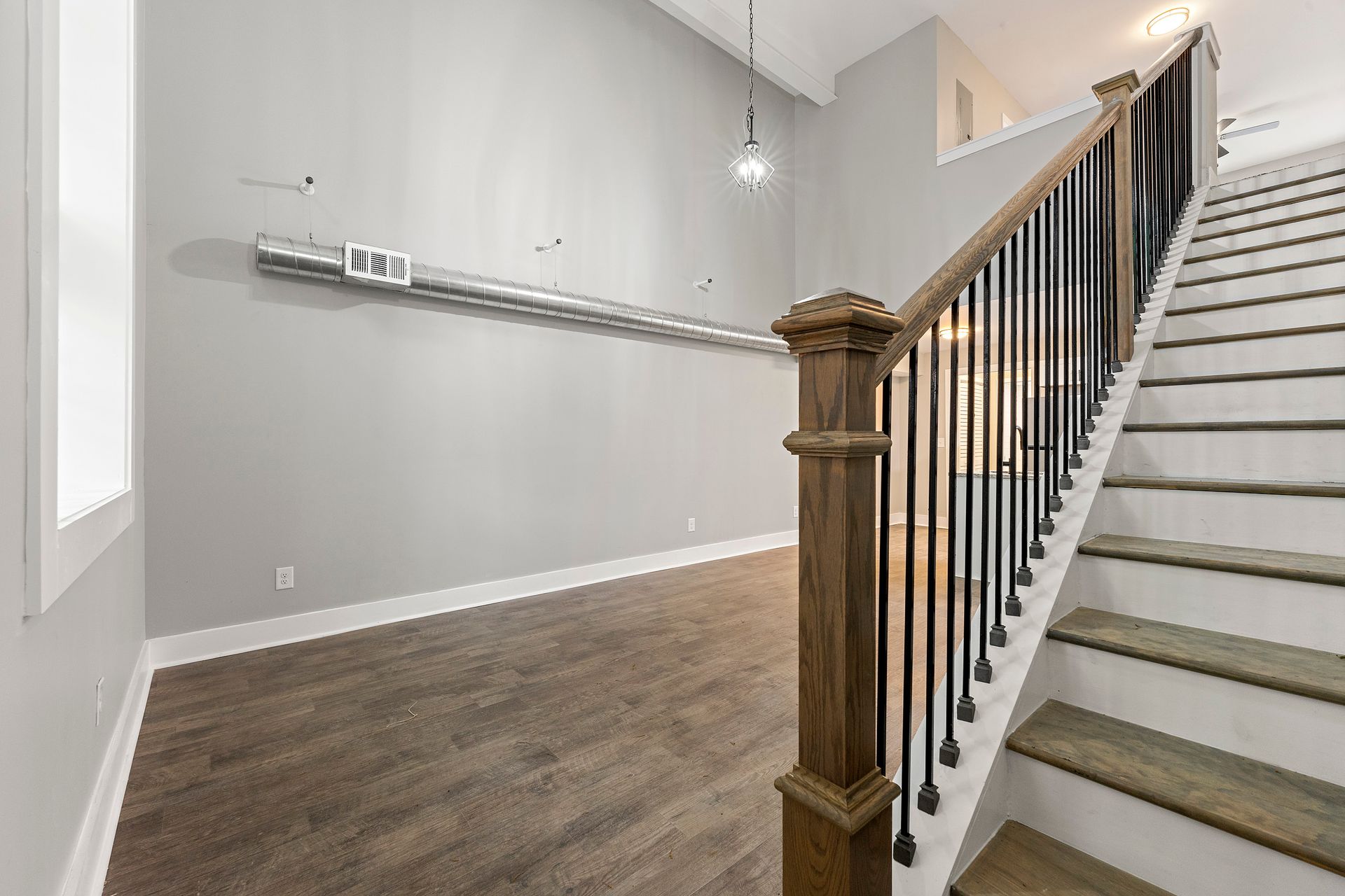 Empty modern room with gray walls, wood floors, and a staircase with white steps and wooden railing