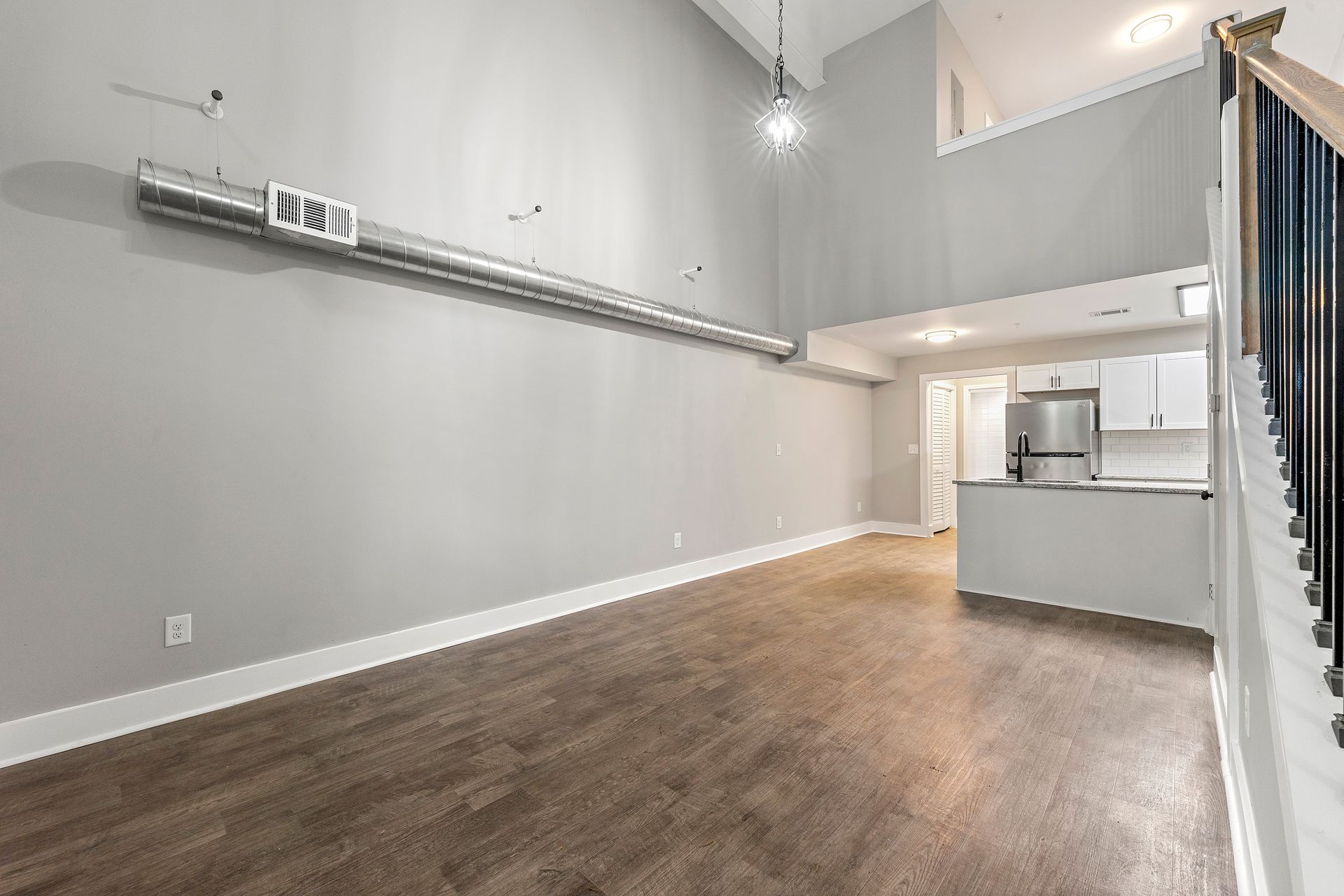 Spacious empty loft with gray walls, wood floors, high ceilings, and an open kitchen area.