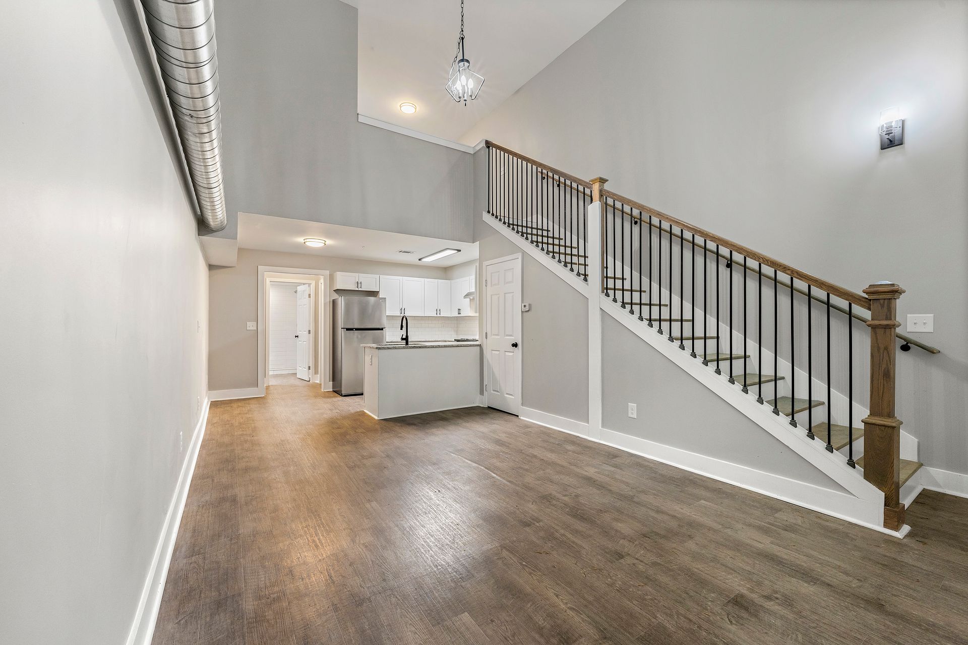 Empty loft-style room with wood floors, white walls, and a staircase with black railing