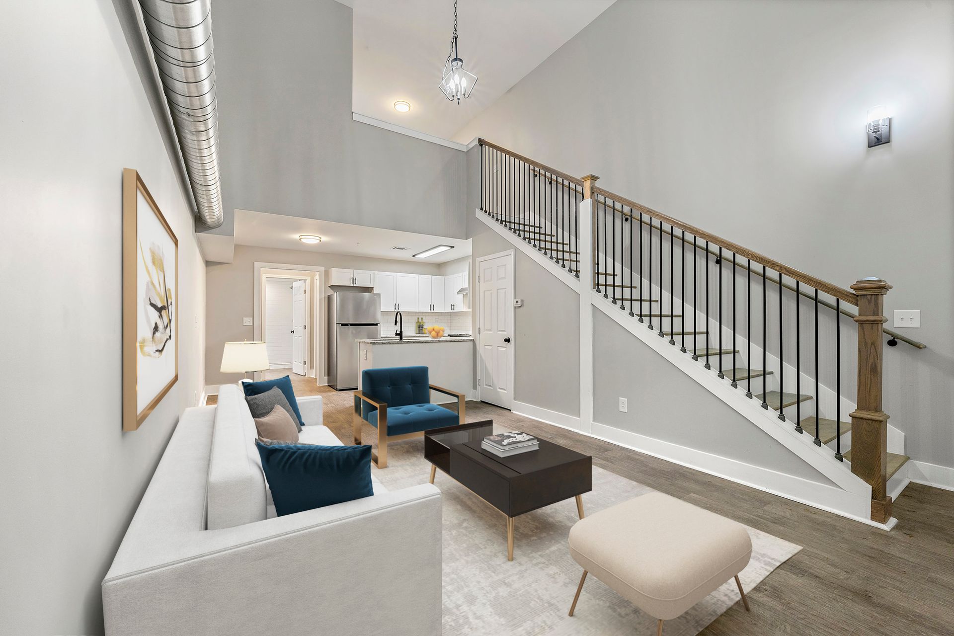 Bright living room with white sofa, blue chairs, coffee table, and staircase leading to an upper loft.