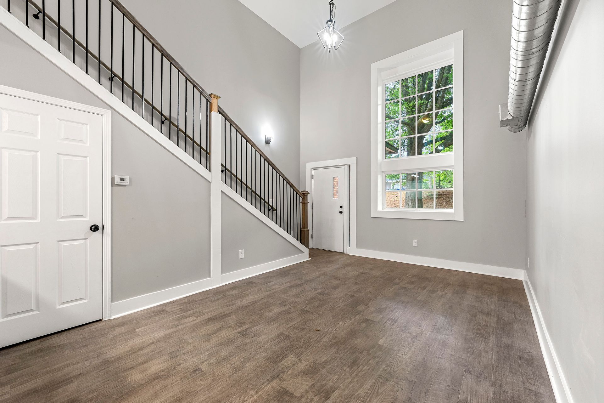Empty gray bedroom with sloped ceiling, white trim, carpeted floor, staircase, and large window