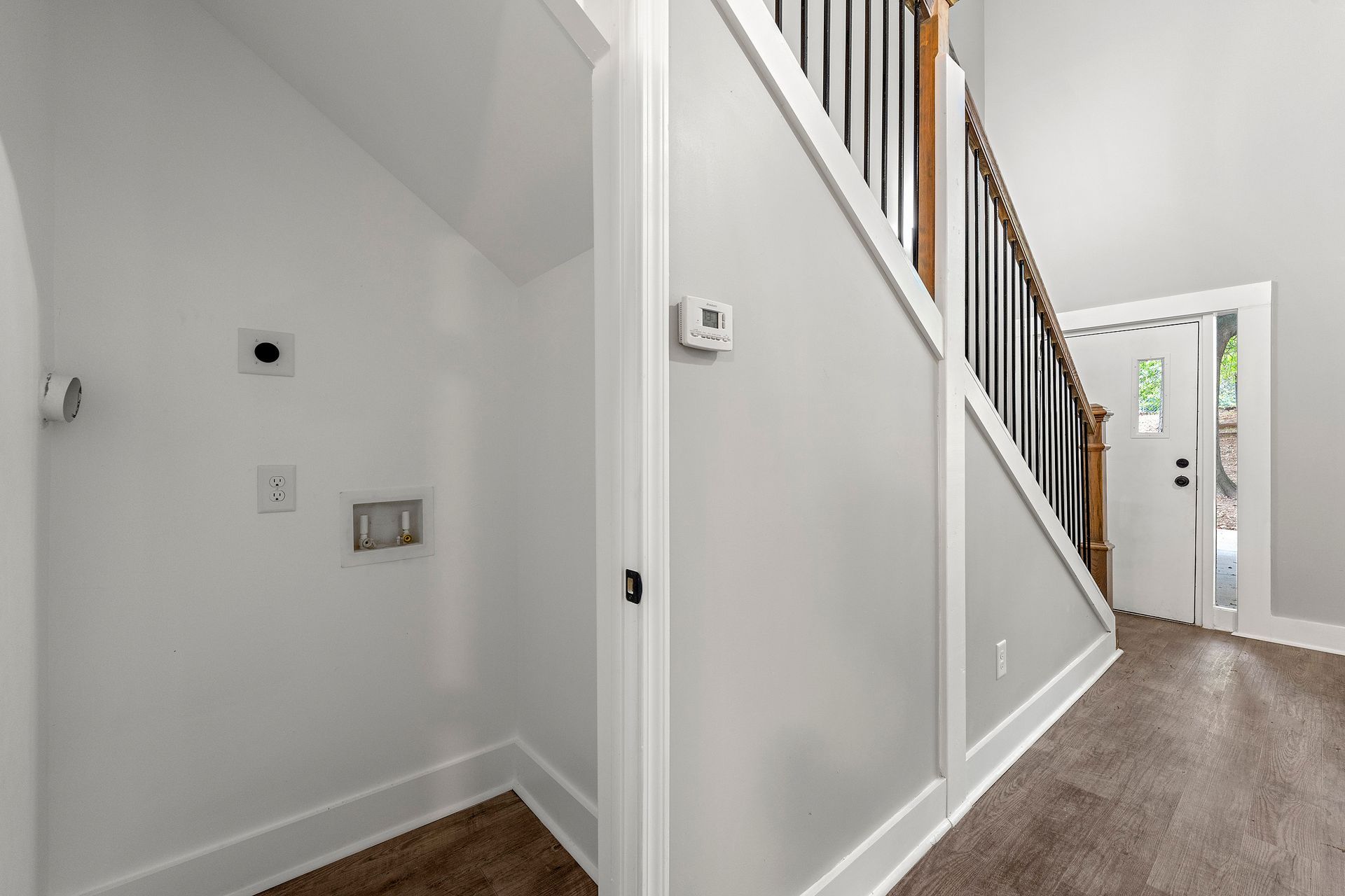 Bright hallway with white walls, carpeted stairs, and a front door in the distance