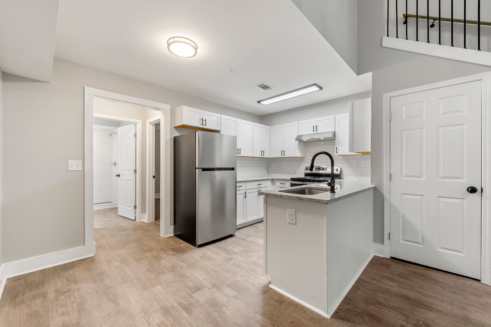 Bright kitchen with stainless steel appliances, white cabinets, and gray walls, viewed from a hallway.