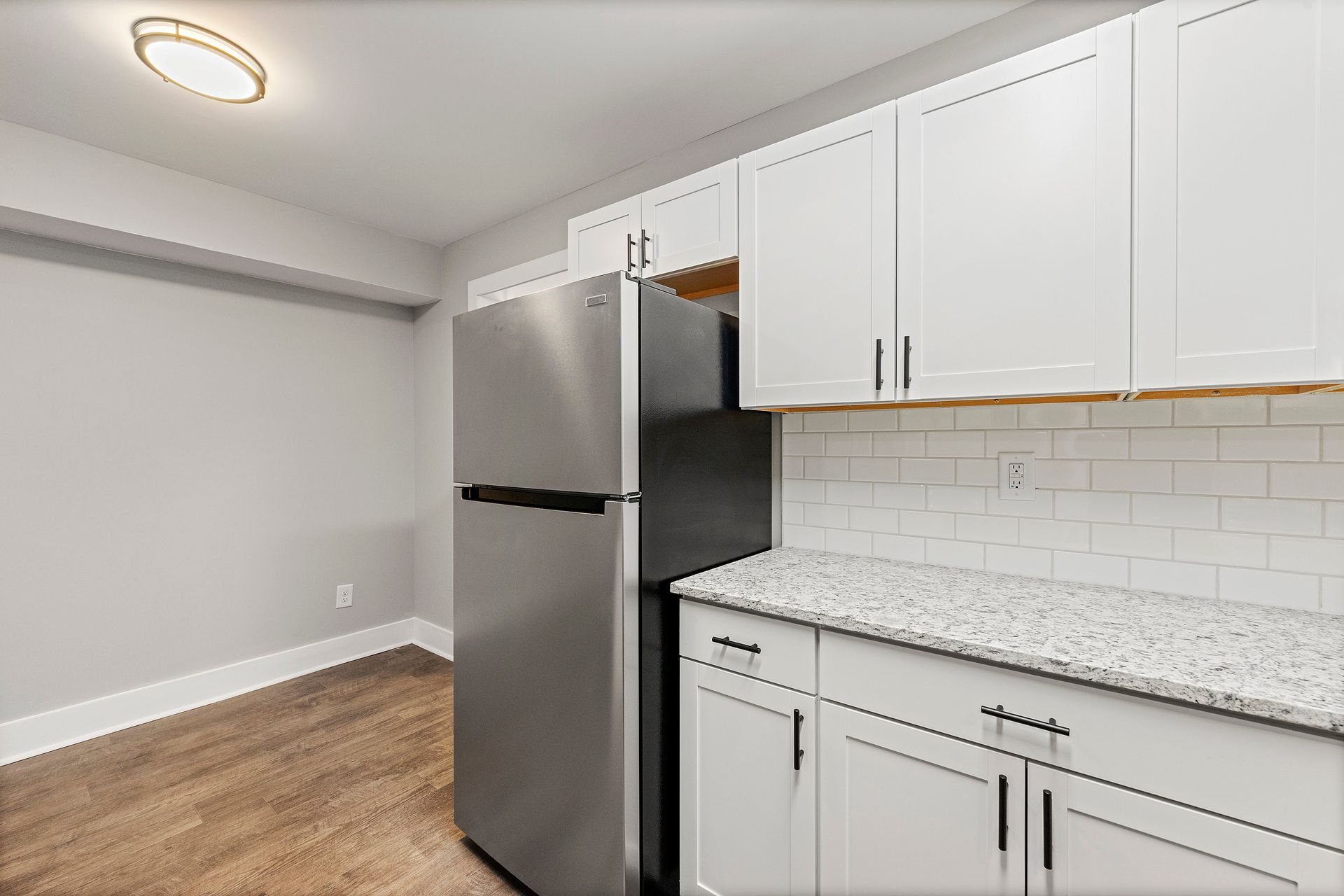 Empty modern kitchen with white cabinets, stainless steel fridge, and gray countertops