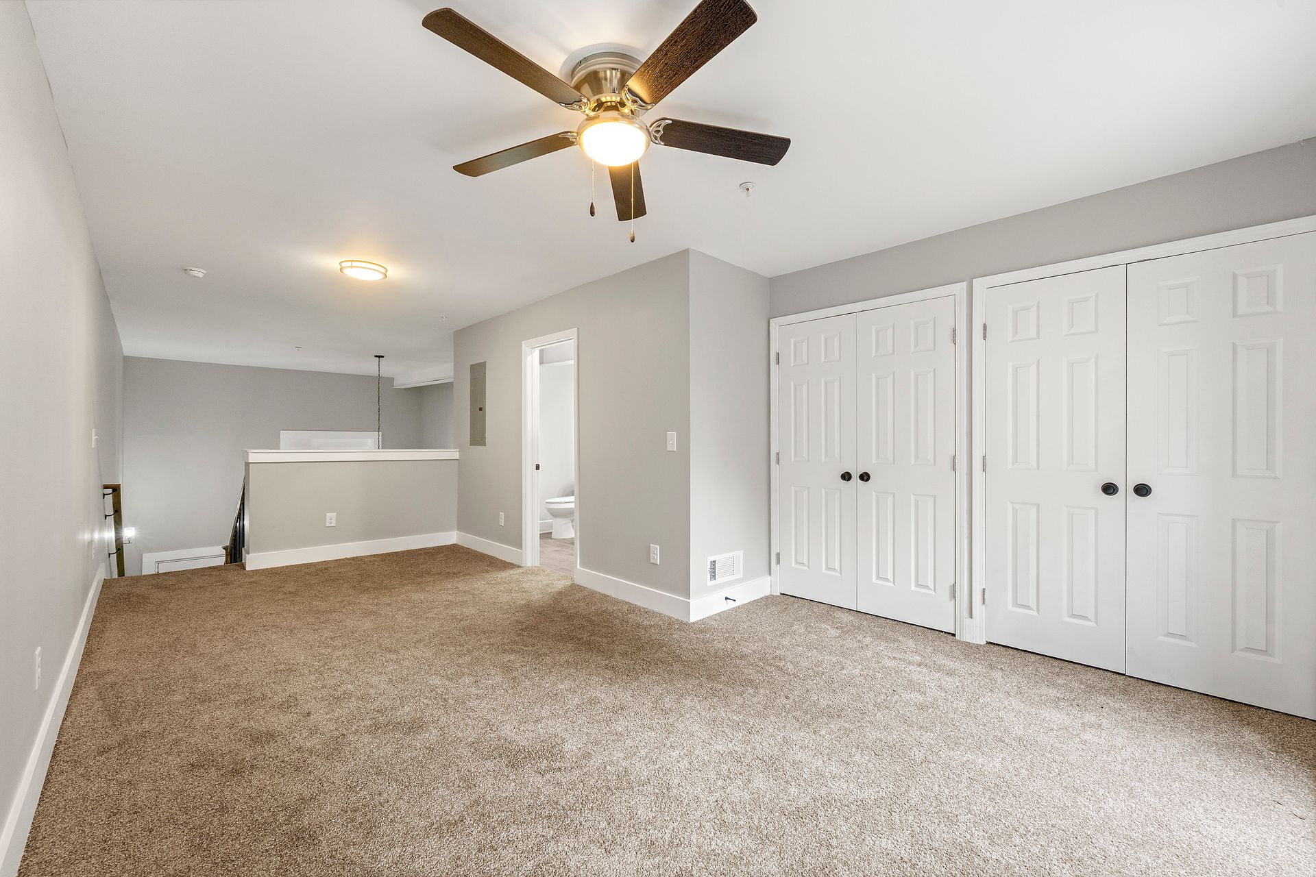 Spacious beige bedroom with carpet, ceiling fan, gray walls, and white closet doors