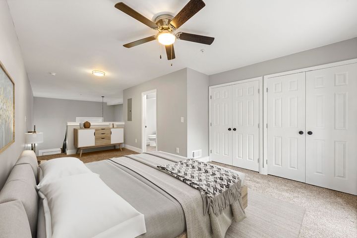 Bright bedroom with a bed, dresser, ceiling fan, and white closet doors on a gray carpet.