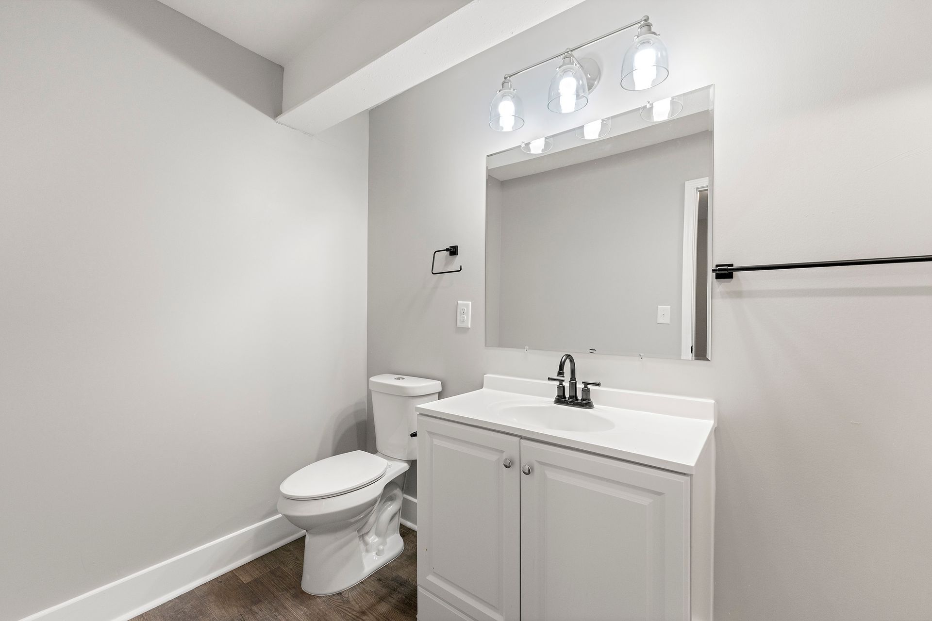 Bright white bathroom with toilet, vanity sink, mirror, and towel bar on the wall.