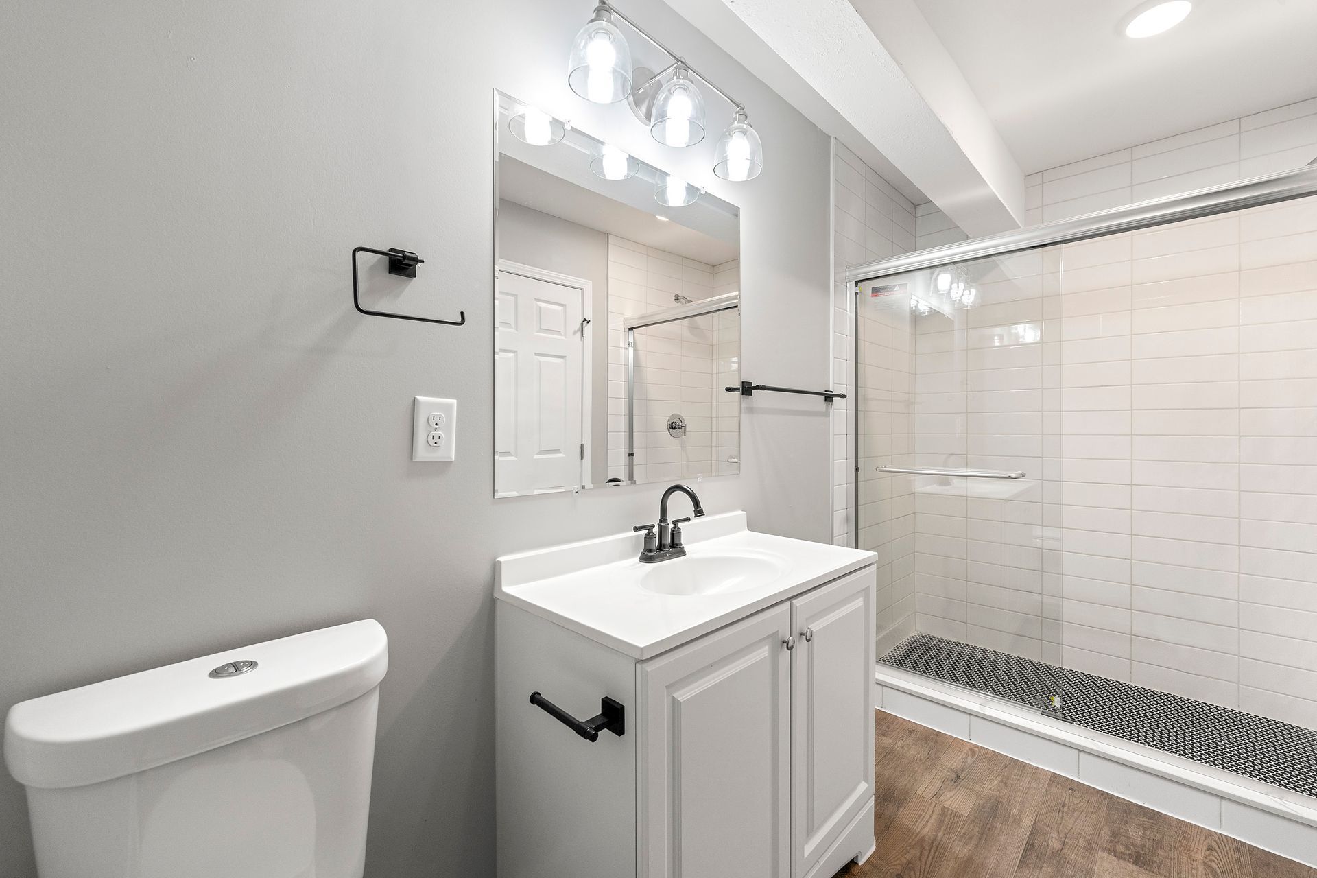 Bright modern bathroom with white vanity, walk-in glass shower, and wood-look floor.