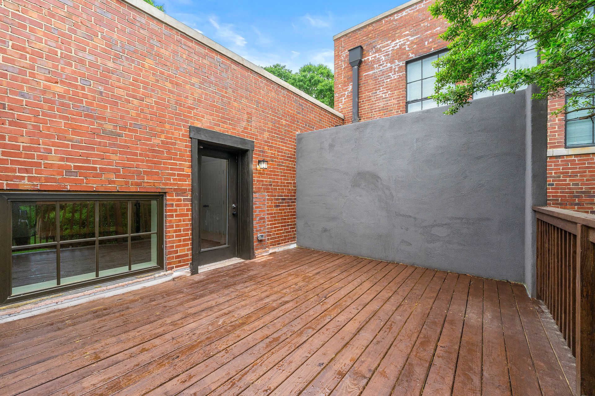 Wooden courtyard deck beside red brick buildings and a gray privacy wall